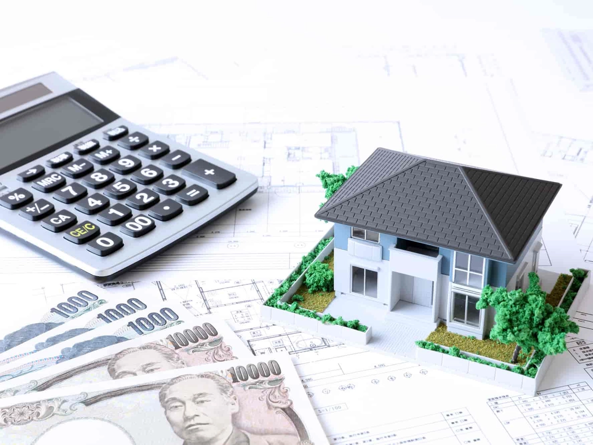 図面の上に置かれた住宅模型と計算機とお金