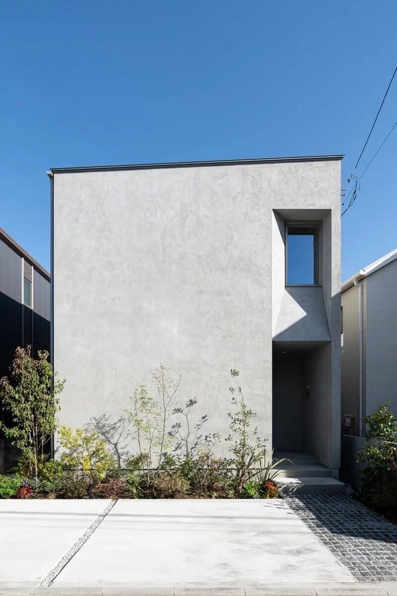 深く窪んだ玄関と窓がある塗り壁の白い箱型住宅