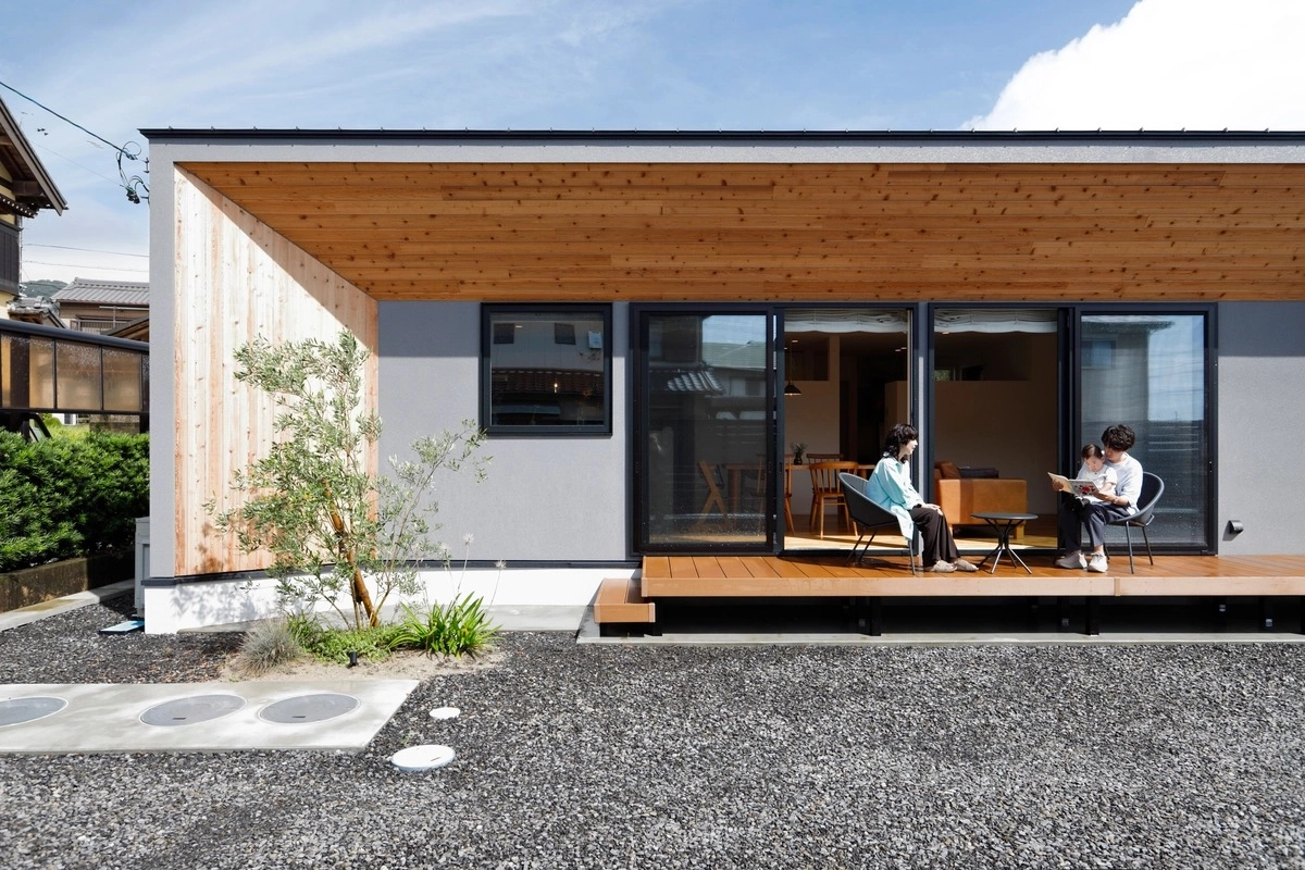 木目の軒下デッキで寛ぐ家族と平屋の外観