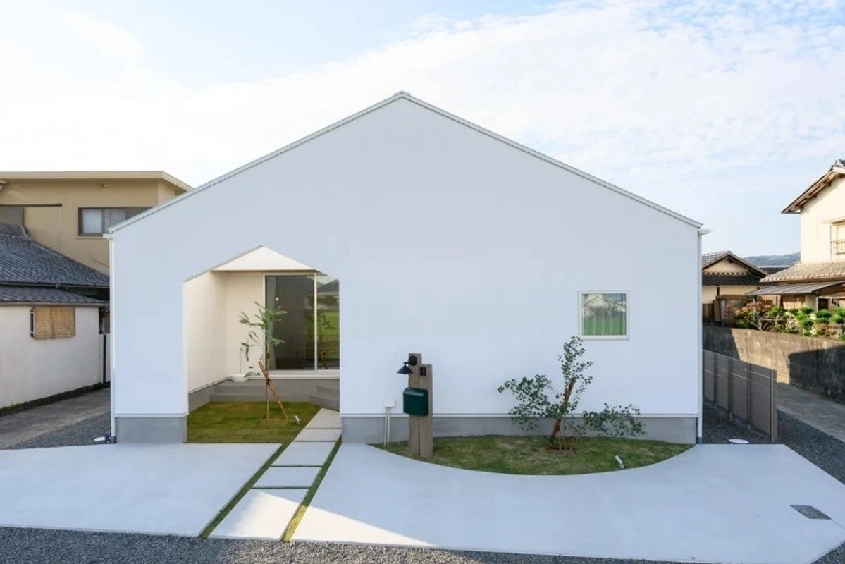 白い切妻屋根が印象的な平屋と、コンクリートのアプローチが続く庭先