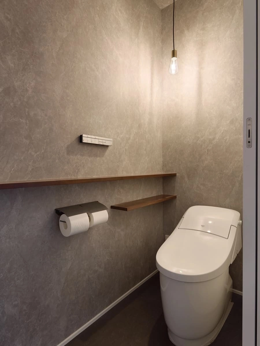 グレーのクロスとペンダントライトの光が落ち着いた雰囲気のトイレ