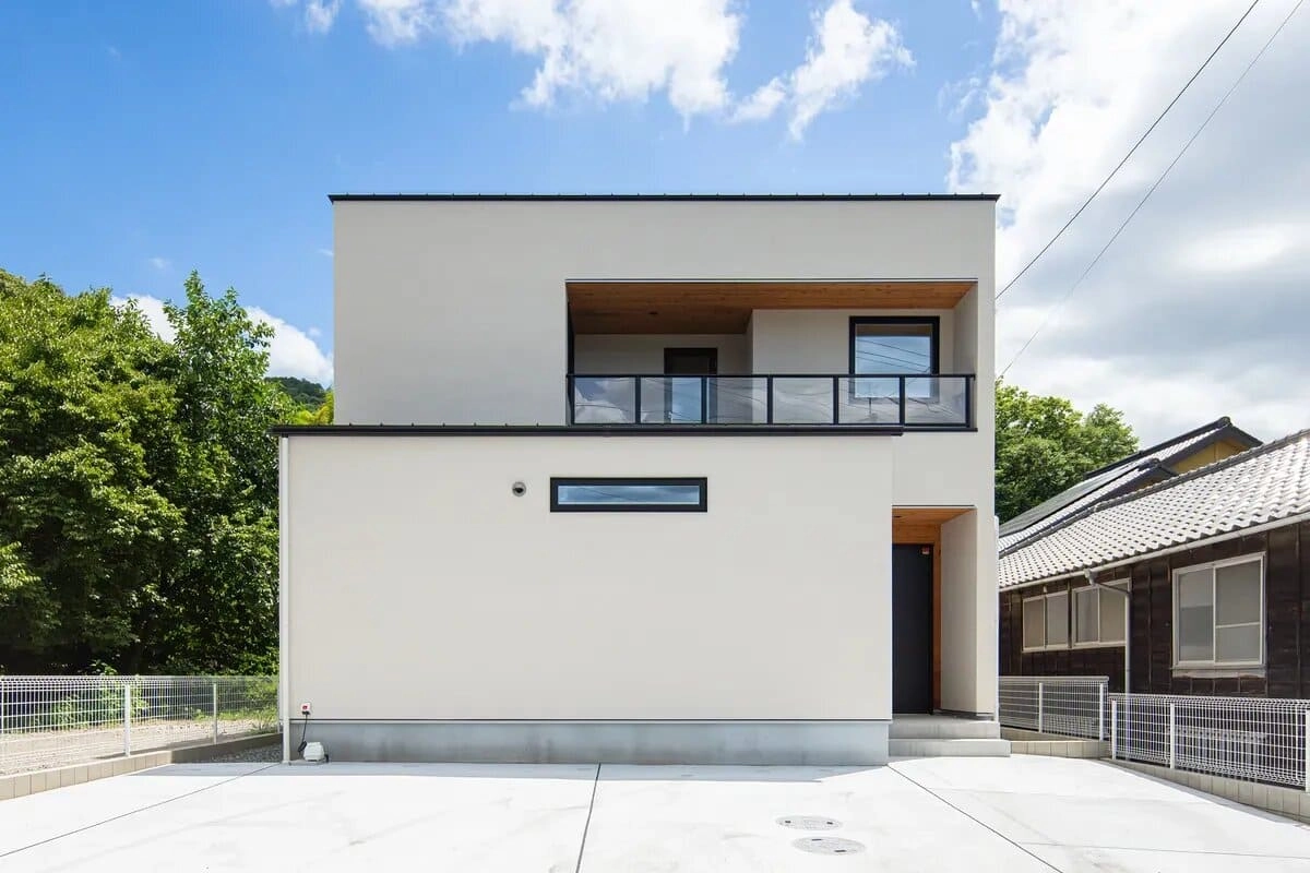 木目天井のバルコニーとガラス手摺がある白い2階建て住宅