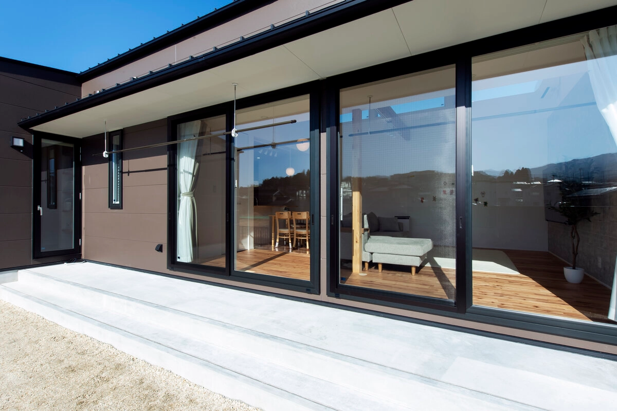 大きな窓からリビングが見える茶色い外壁の住宅