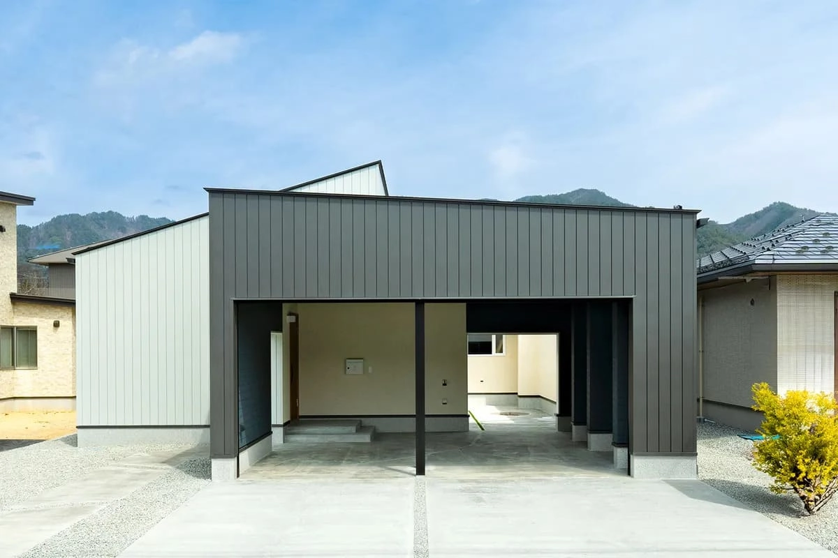 山を背景にしたダークグレーの外壁と広いガレージのある住宅