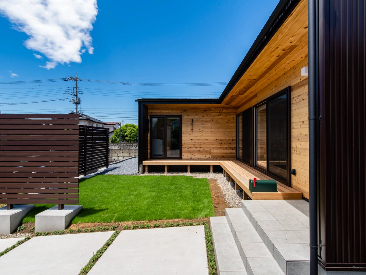 庭がフェンスで囲われた黒と木目の外観