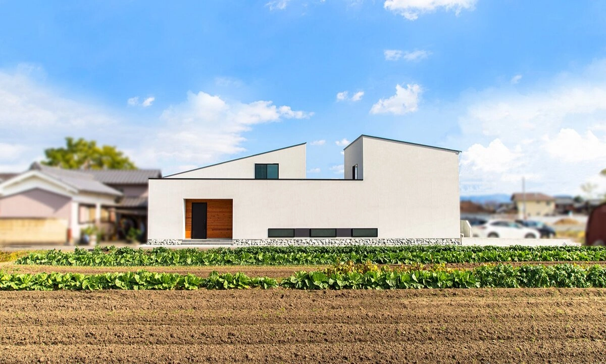 畑の奥に佇む白い塗り壁と木目アクセントのモダンな平屋
