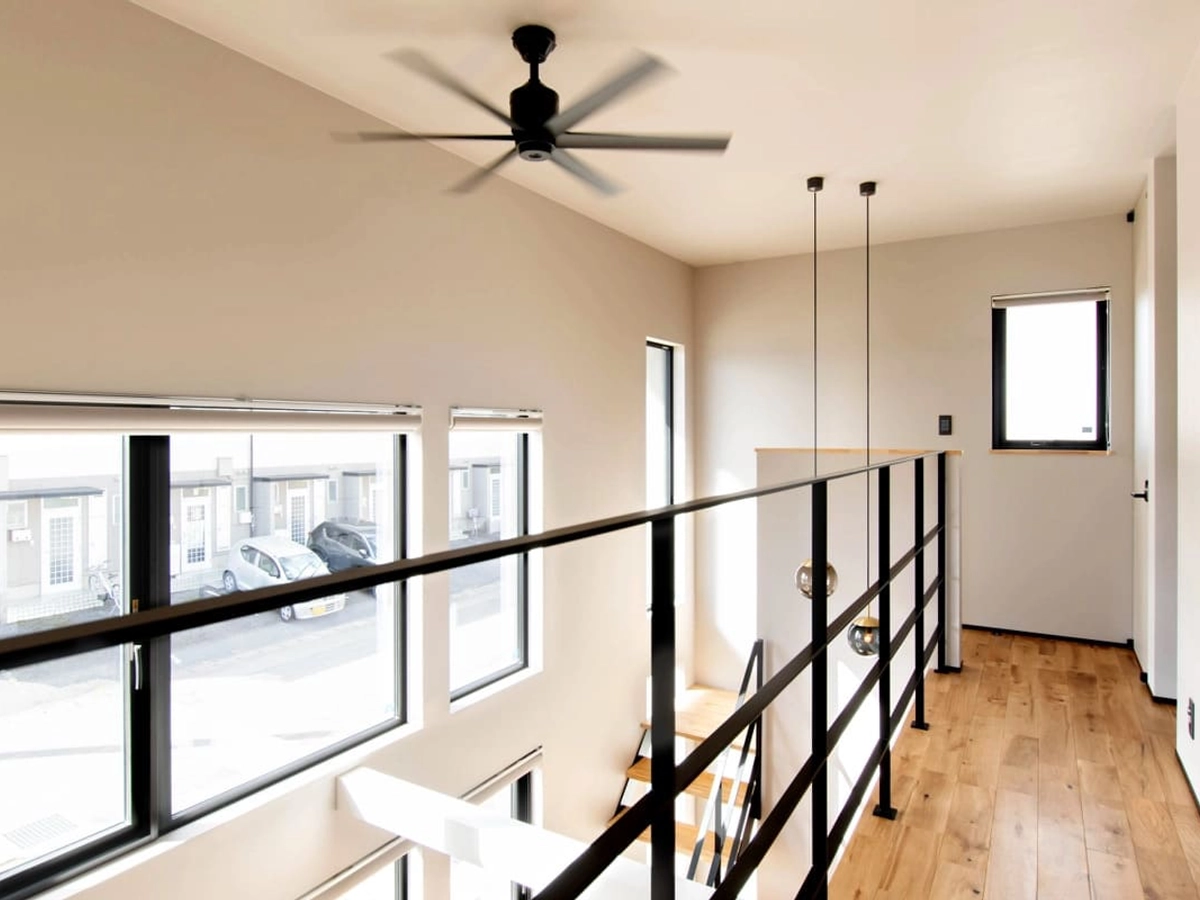 黒いシーリングファンのある吹き抜け2階から見える窓の景色