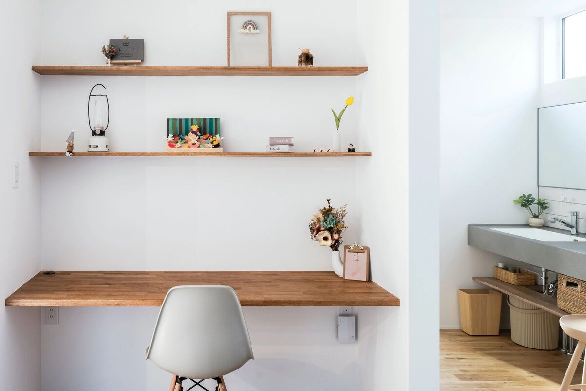白壁に木製棚を設えた、お気に入りの雑貨を飾るシンプルで温かみのある書斎デスクスペース