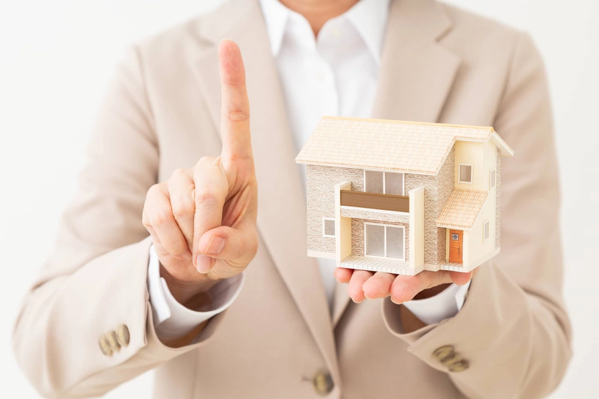住宅模型を持って人差し指を立てるスーツ姿の人