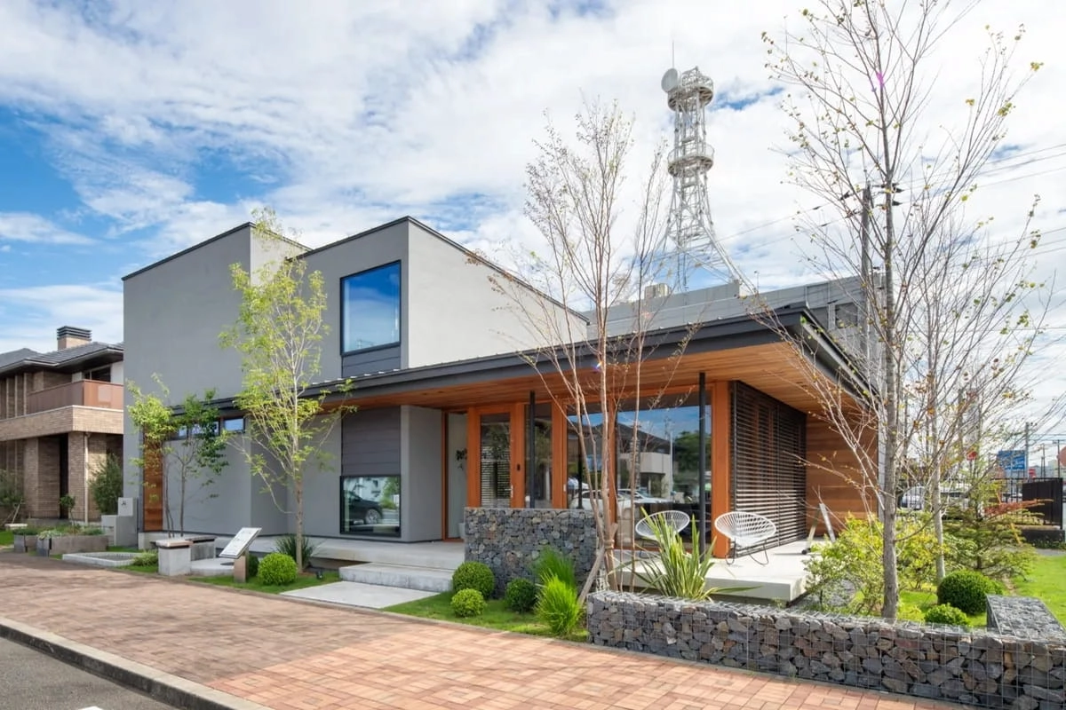 電波塔を背にした石積みの壁と深い軒があるグレーの住宅