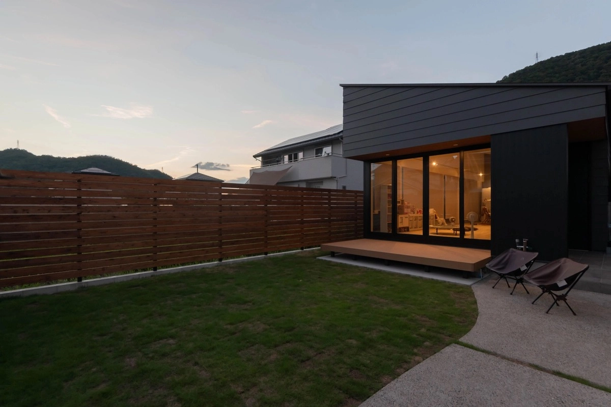 夕暮れ時の芝生の庭とウッドデッキがあるモダンな住宅