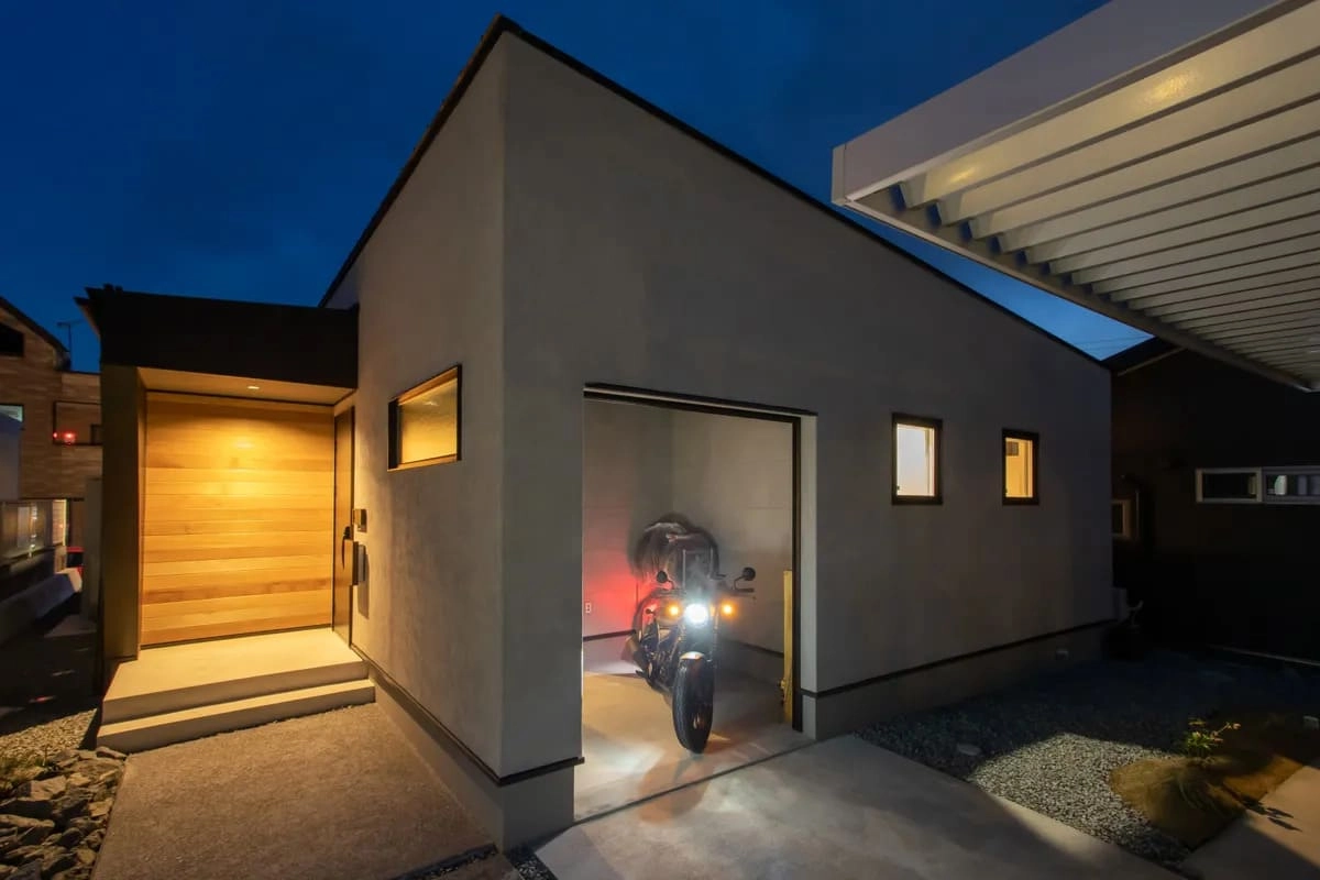 ライトを点灯したバイクが停まる夕暮れ時のガレージ付き住宅