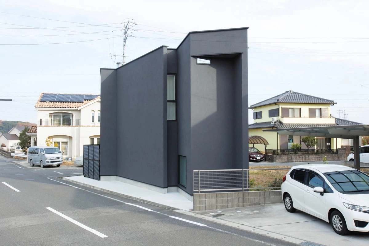 道路脇に建つ特徴的な外観の濃グレーの家