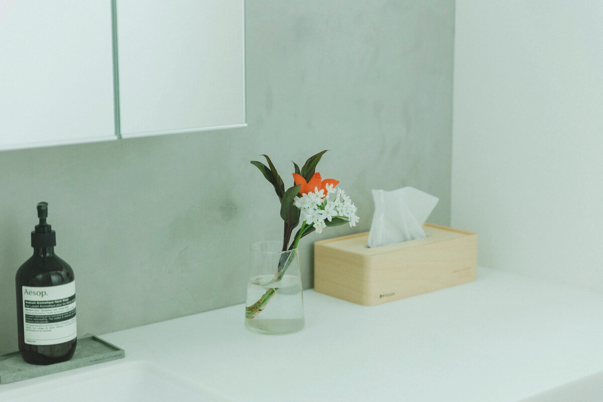 白い洗面台に置かれた花瓶とハンドソープと木製ティッシュケース
