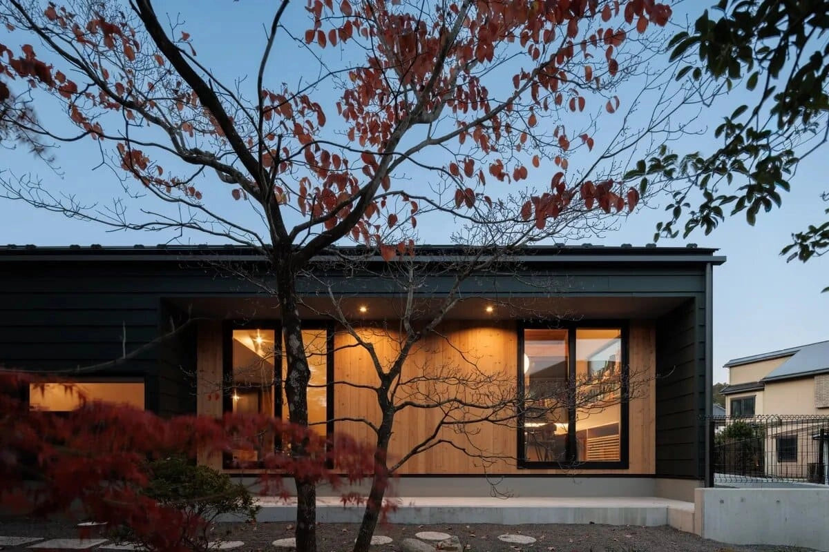 紅葉した木立越しに見える大きな窓と板張り外壁の平屋