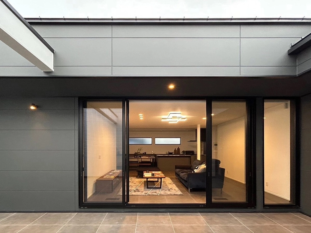 大きな窓から暖かい光が漏れる夜のモダンなリビングとテラス