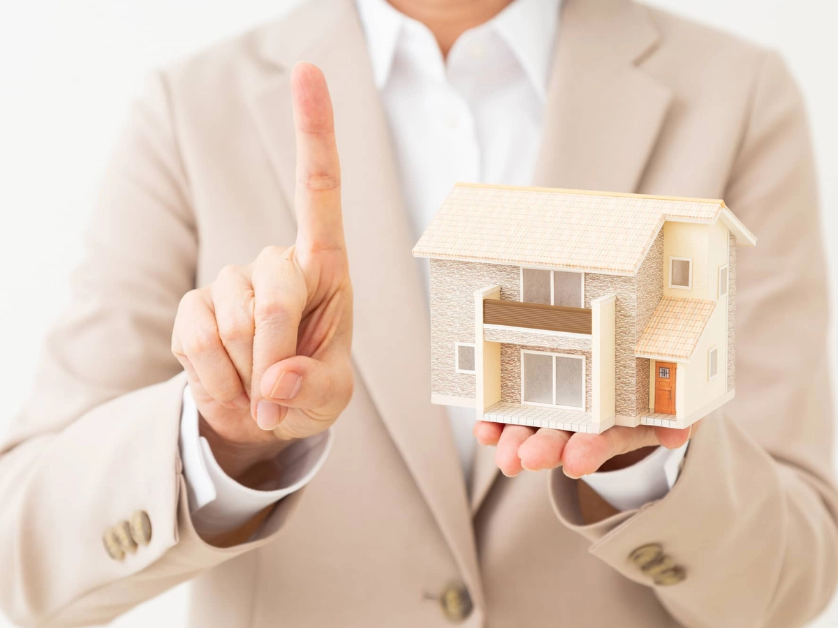 戸建て住宅の模型を持って人差し指を立てるスーツ姿のミドル女性
