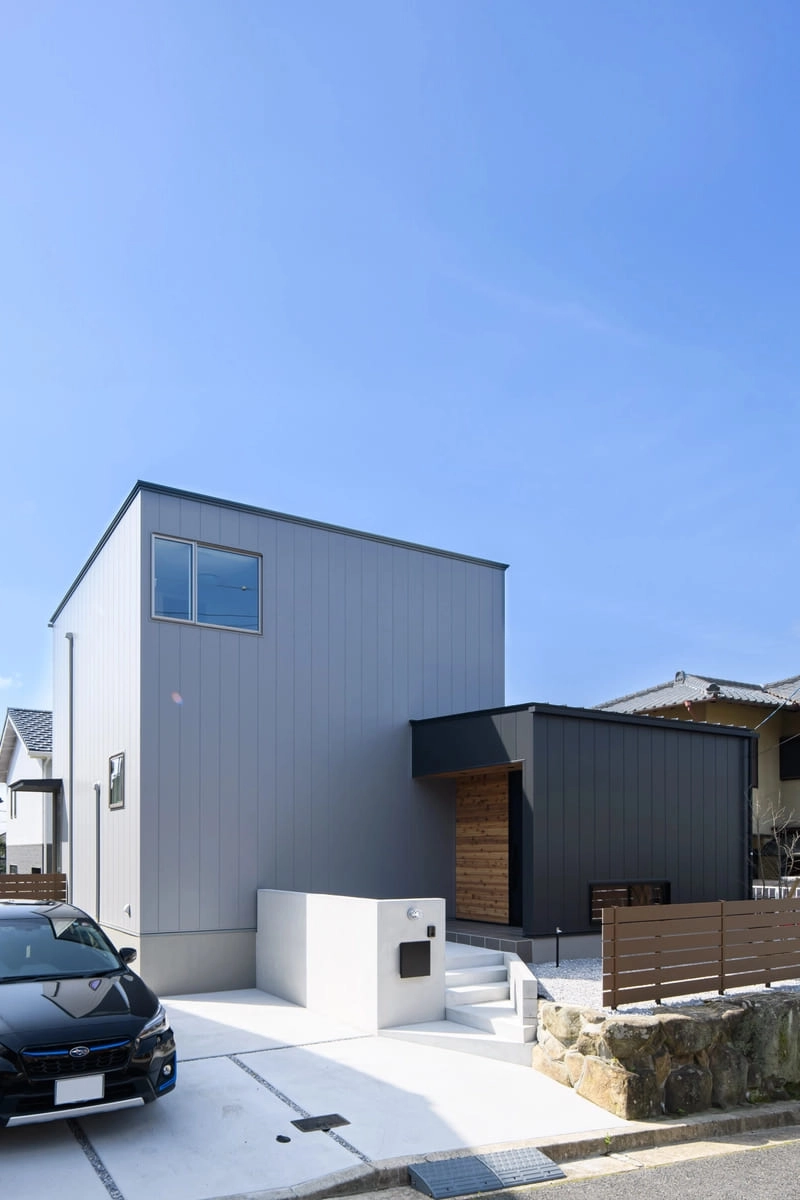階段の玄関アプローチが設置された明るいグレーの箱形住宅