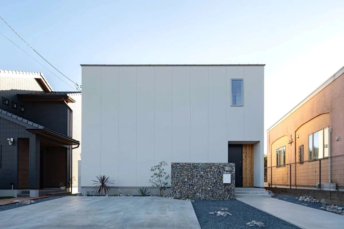 石積みの門柱と砂利敷きの駐車場がある白い箱型の住宅