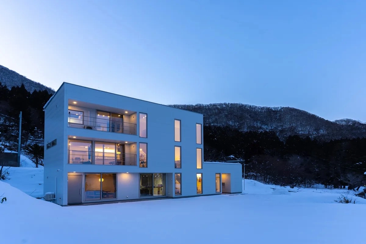 雪原に佇む夜の光に照らされた三階建ての白いデザイナーズ住宅