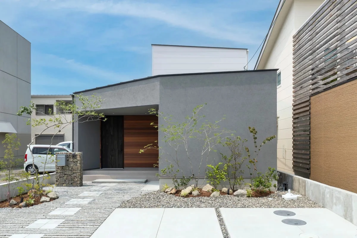グレーの塗り壁と木製ドアがスタイリッシュな住宅外観