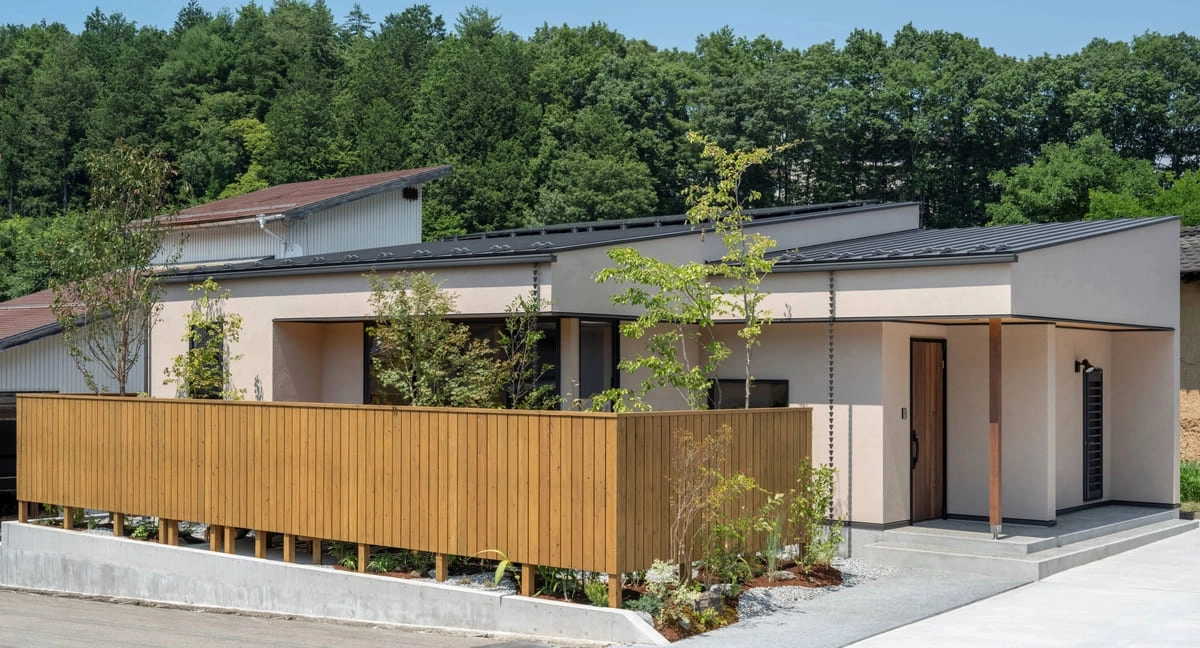 低い木製フェンスと植栽に囲まれた平屋風のモダンな外観
