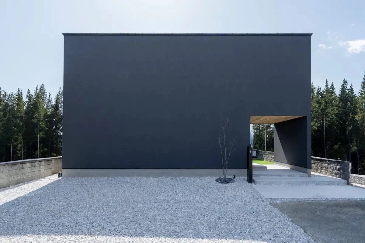 深い森を背景にした右下に抜けのある黒い箱型の住宅