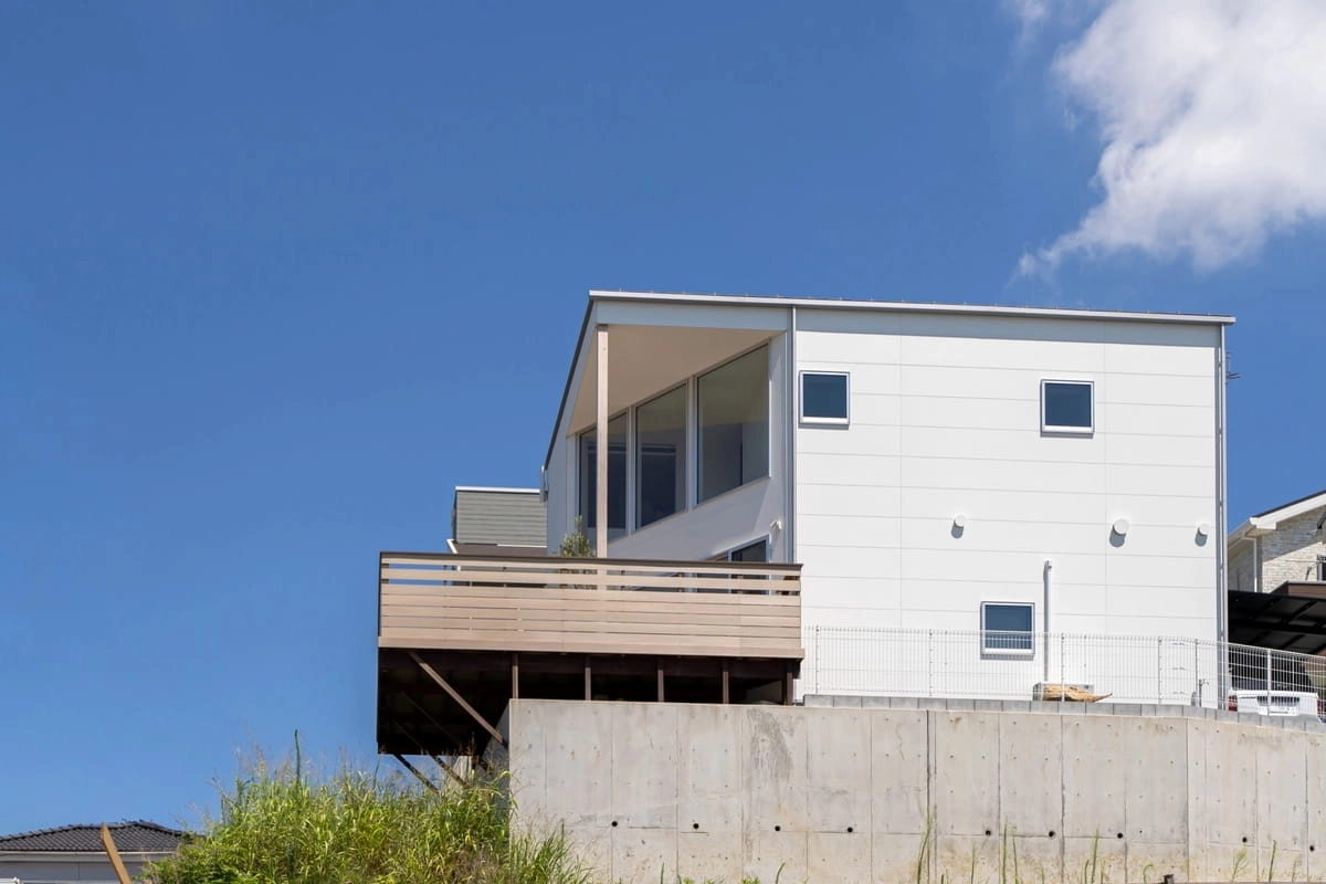 コンクリート擁壁の上に建つウッドデッキのある白い住宅