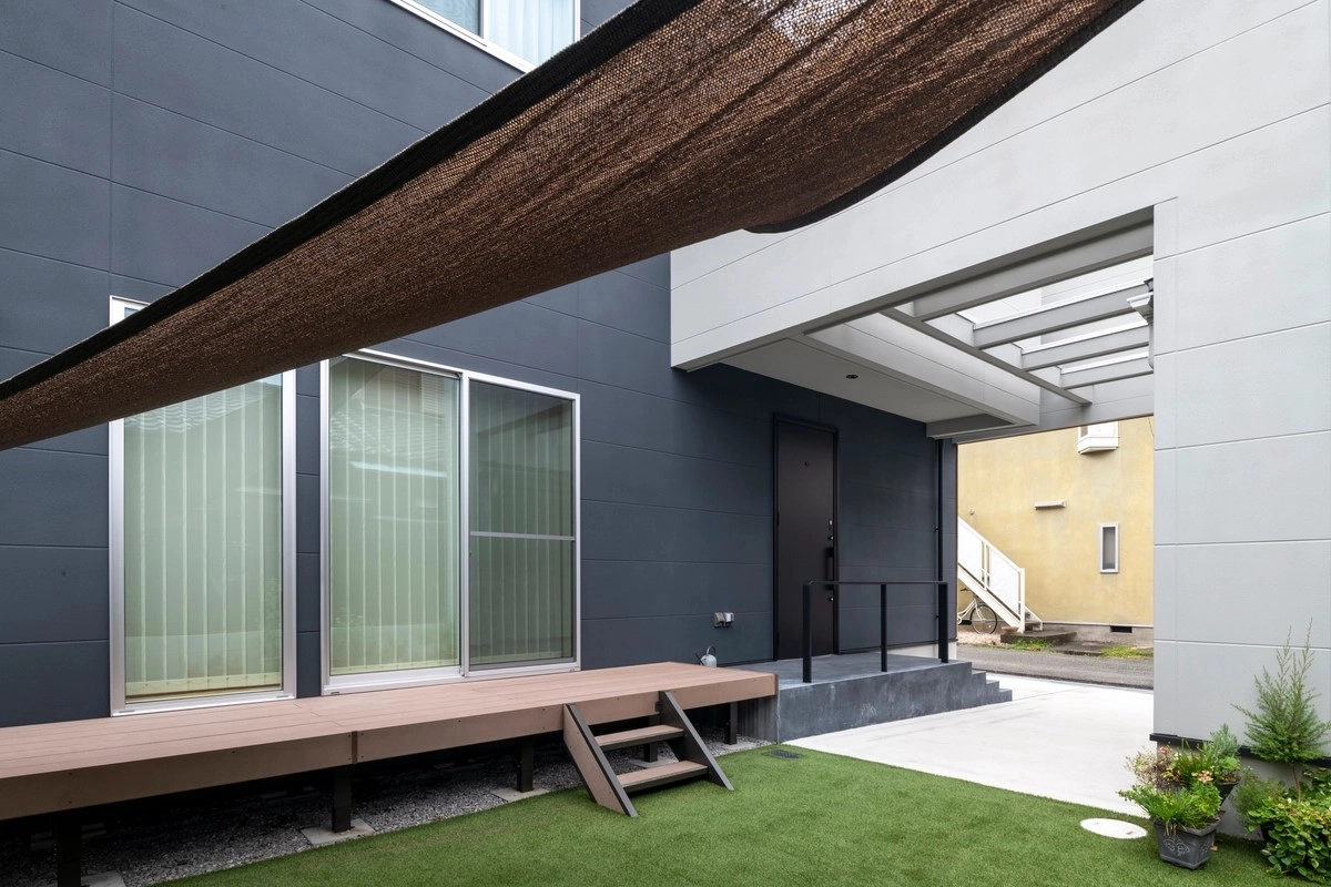黒い外壁にウッドデッキと人工芝が映える中庭と日よけシェード