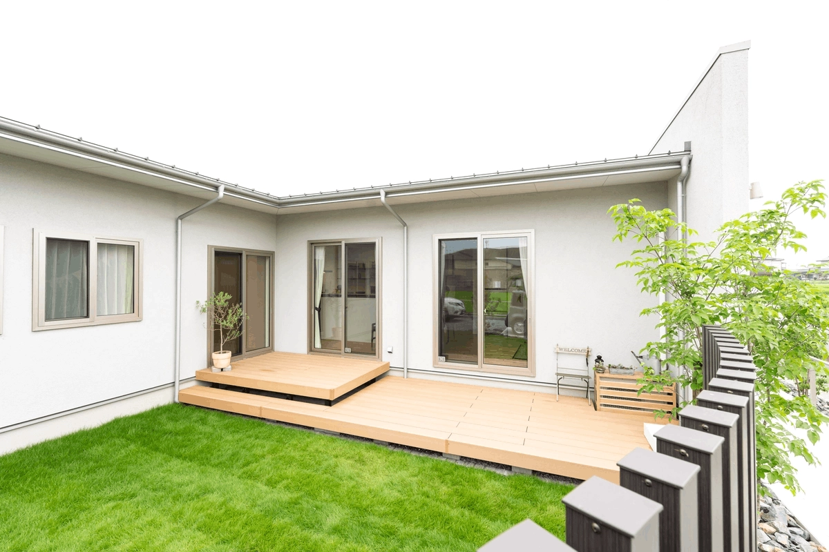 芝生の庭とウッドデッキを囲むL字型の平屋外観
