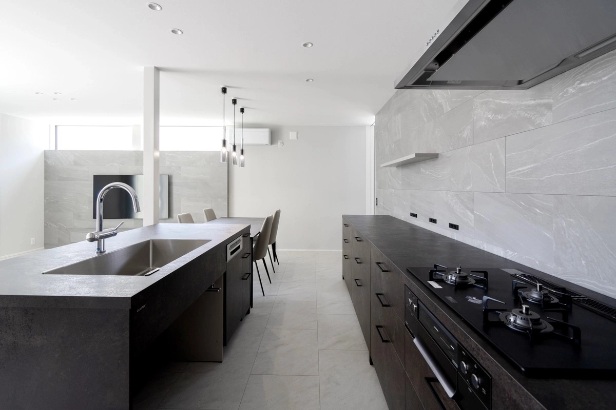 大理石調の壁タイルとダークトーンのシステムキッチンが調和した開放的なアイランドキッチン