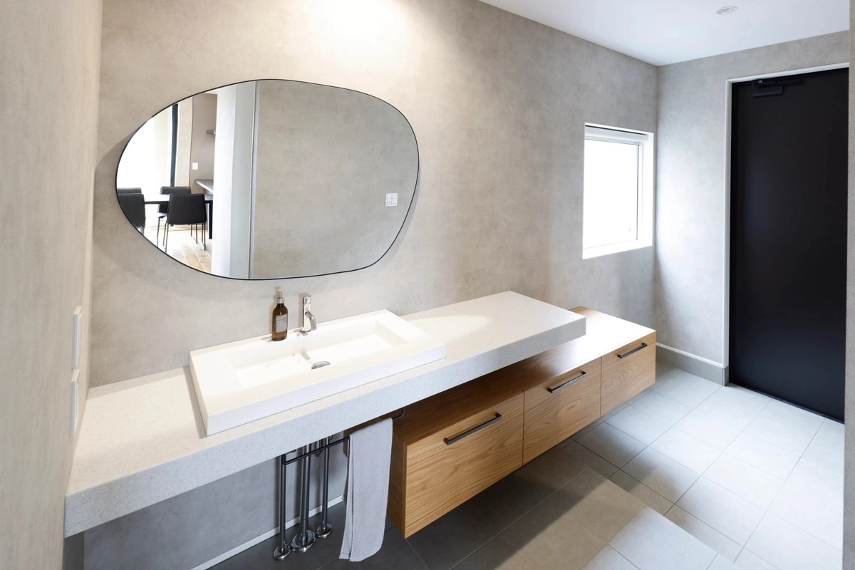 ベッセル式洗面器と大きな変形ミラーを配したモダンな洗面所