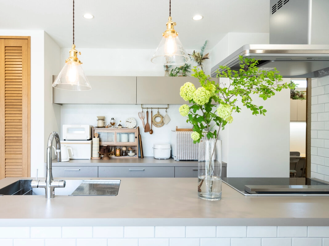 真鍮のペンダントライトが灯る、グレーのワークトップと白タイルがおしゃれな対面キッチン