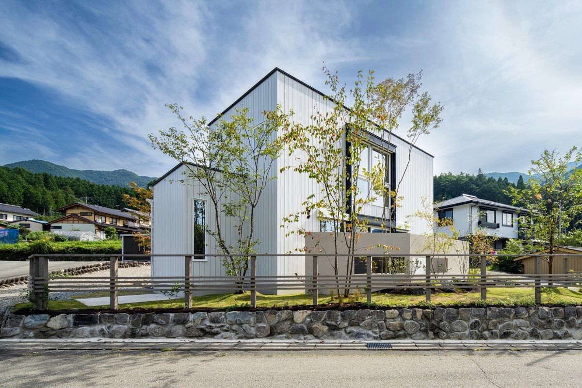 山並みを背に植栽が映える白い外壁のモダンな二階建て住宅