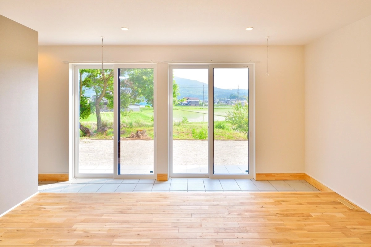 大きな掃き出し窓から田園風景を望む明るい無垢床の室内