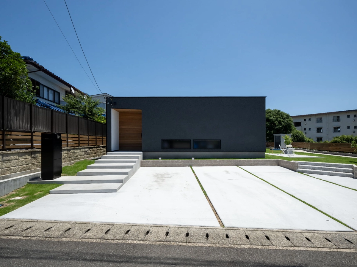 広い駐車場のあるシンプルな黒い平屋の家