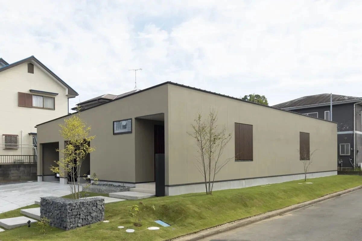 芝生のアプローチと石積みの門柱があるベージュの平屋