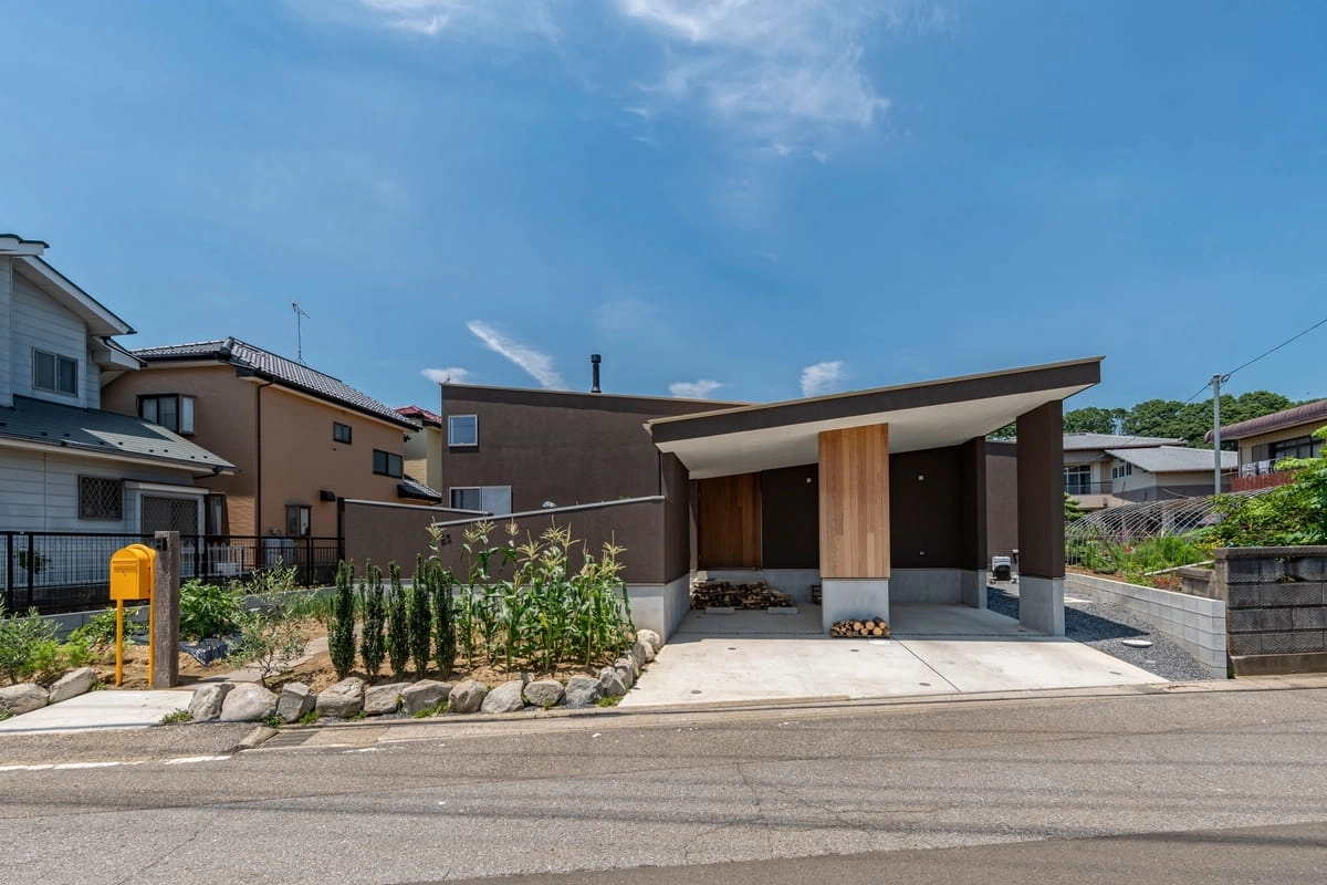 畑と薪置き場のある片流れ屋根の茶色い平屋