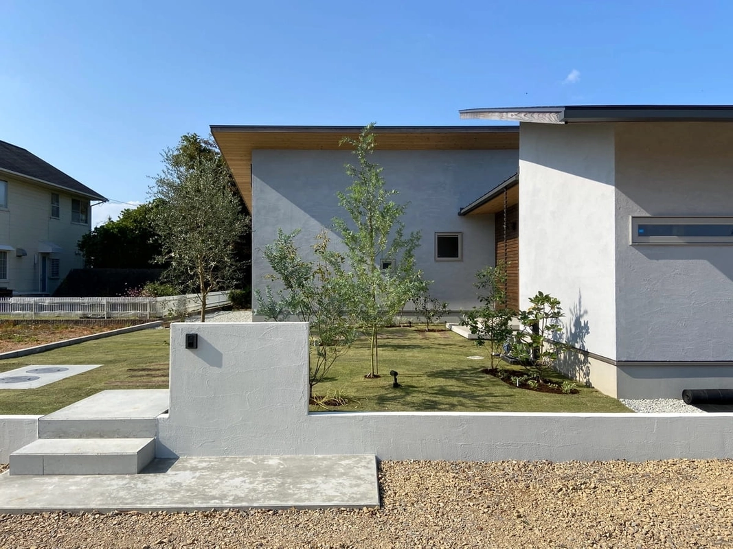 芝生の庭と植栽が広がる深い軒のある白い平屋