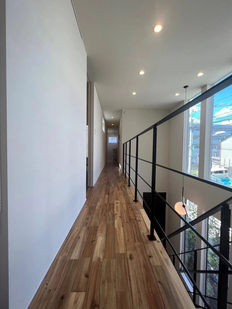 吹き抜けに面した黒いアイアン手すりの廊下と温かみのある無垢床の質感