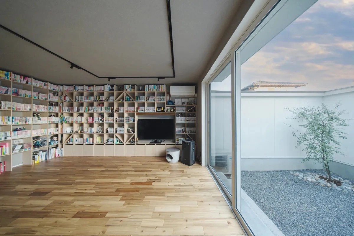 壁一面の書棚に漫画が並ぶ中庭に面した開放的なリビング