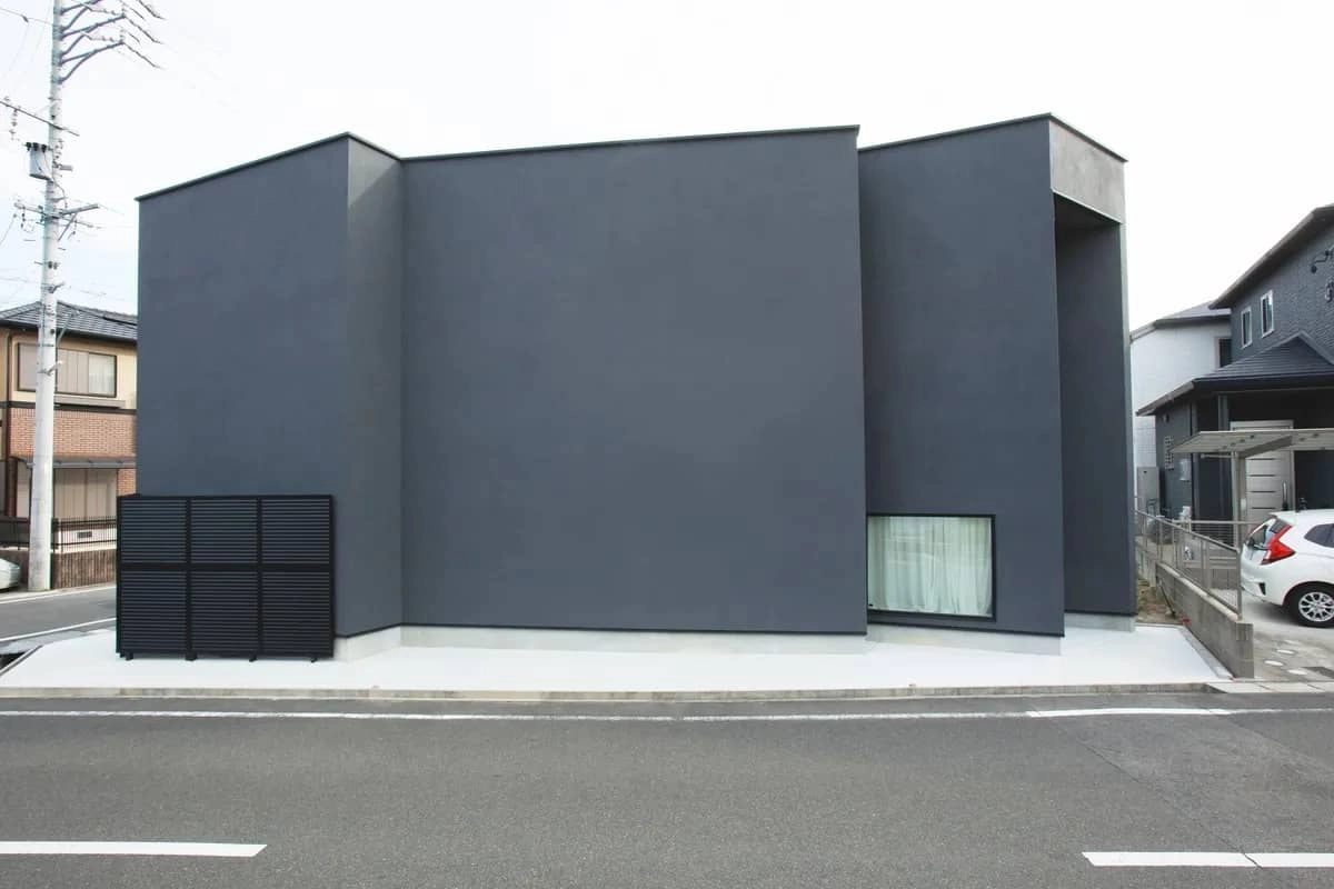 黒いルーバーがあるグレーの箱型のモダンな住宅