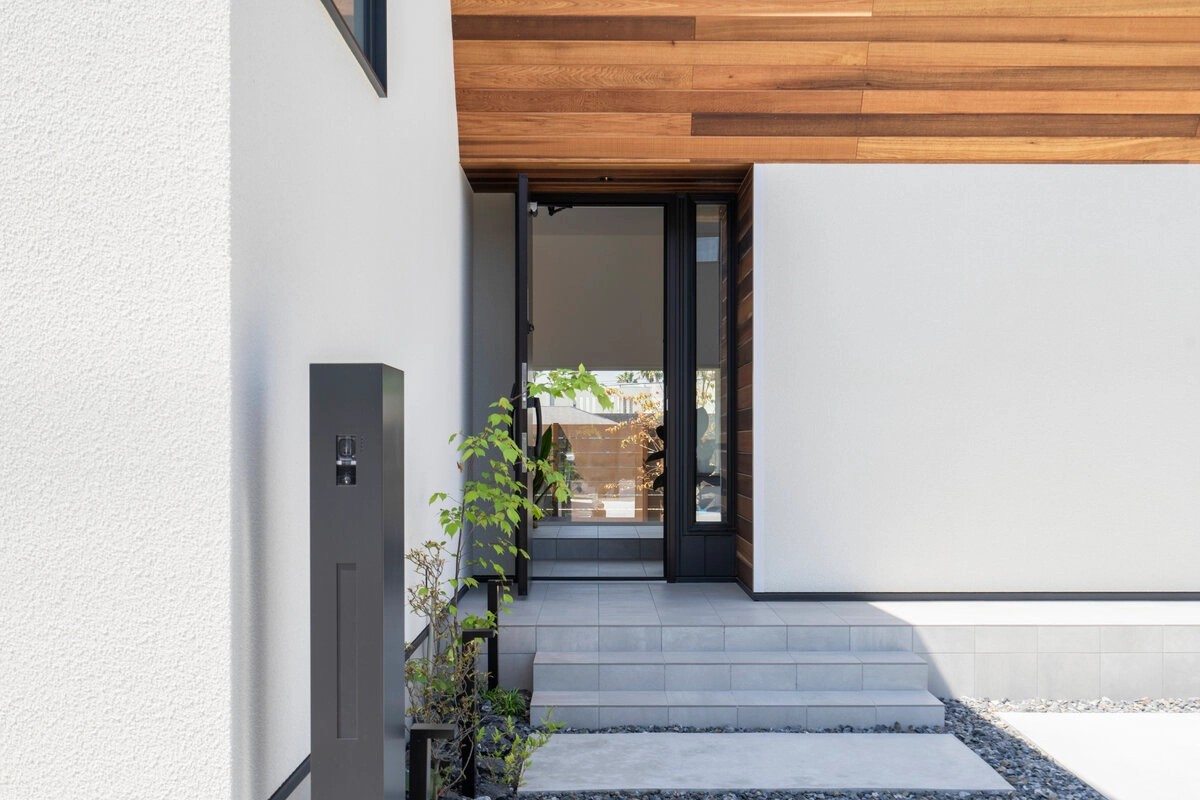 白い外壁と板張りの軒天が特徴的なガラスドアの玄関