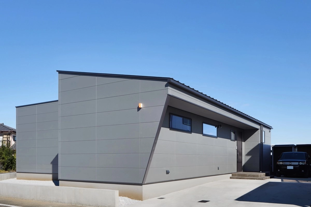 青空の下に佇むシャープな斜め壁が特徴的なグレーの平屋の外観