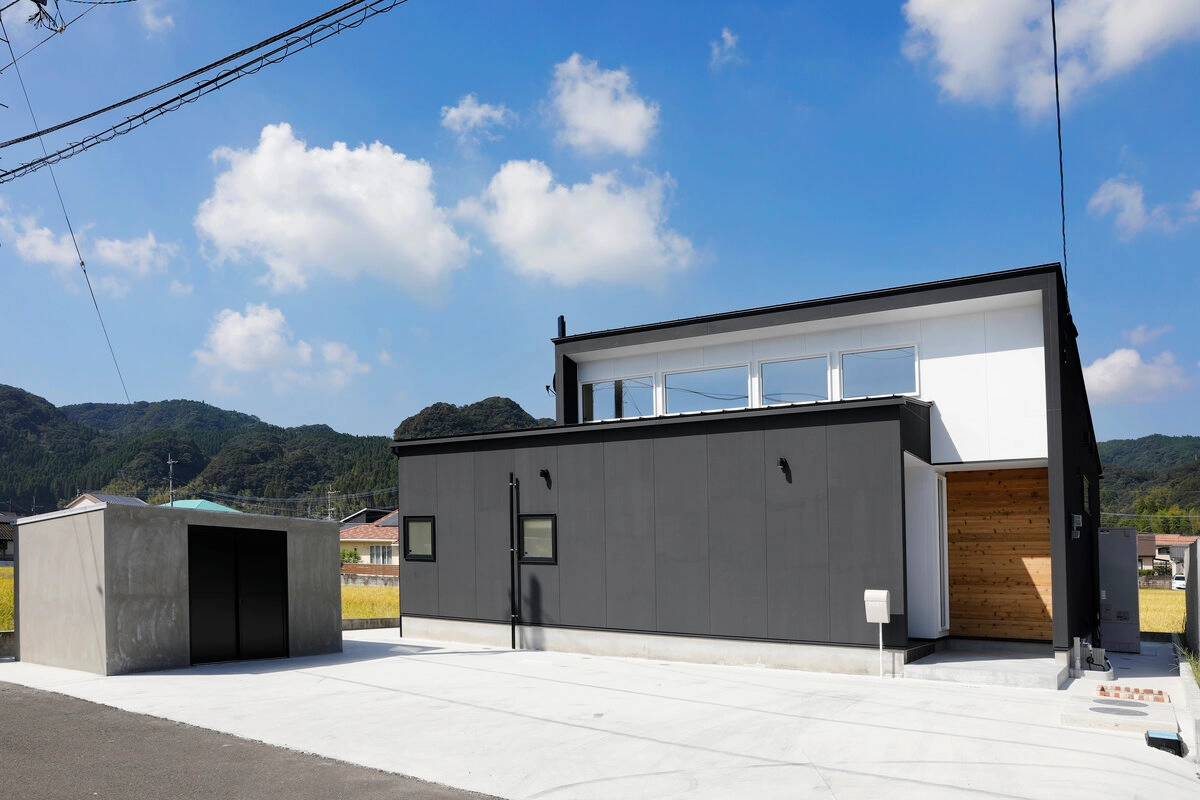 青空と緑豊かな山々を背景にしたモダンな黒い住宅の外観