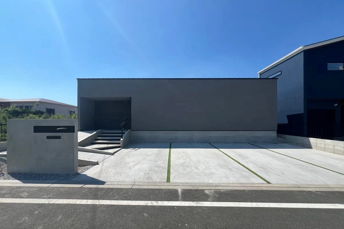 コンクリートの駐車場とスロープがあるグレーの箱型住宅
