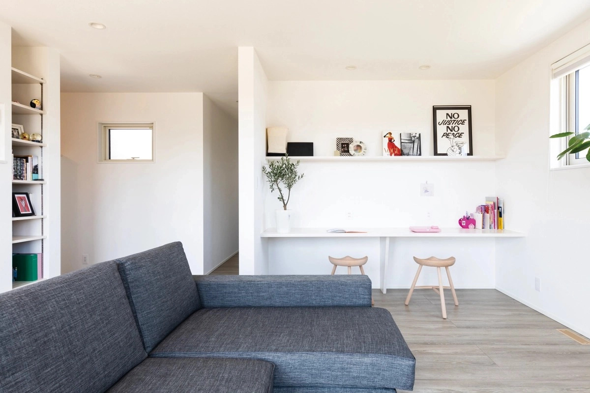 造作デスクとグレーのソファを配置した白いリビング