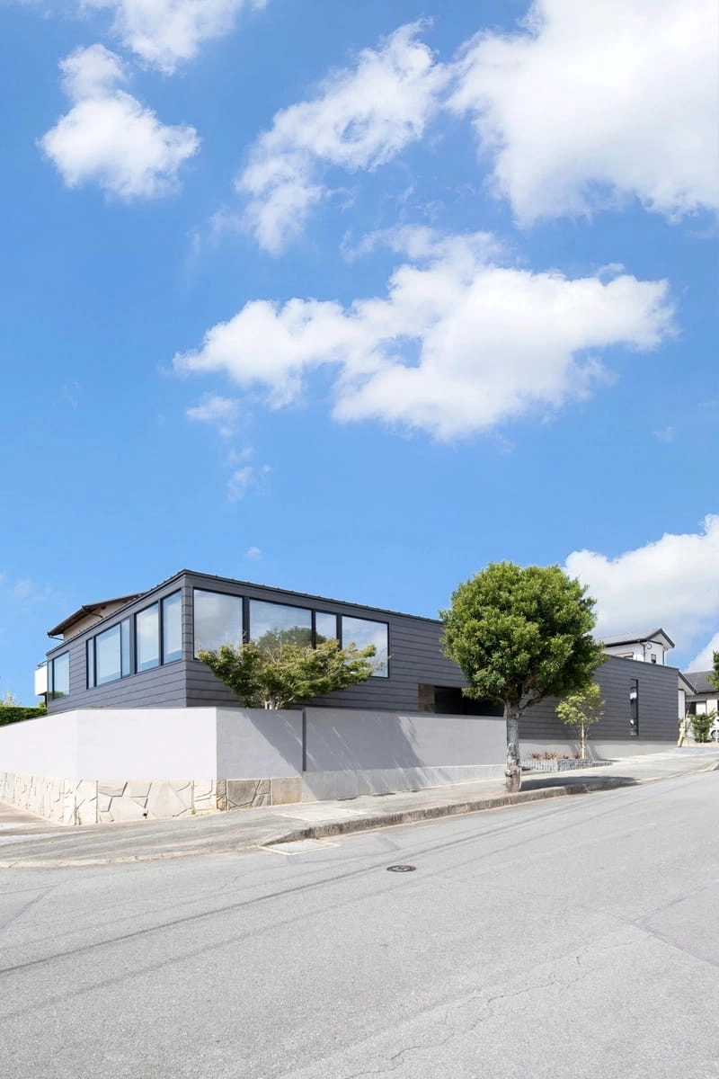 青空を反射する横長の連続窓があるグレーの外壁の平屋