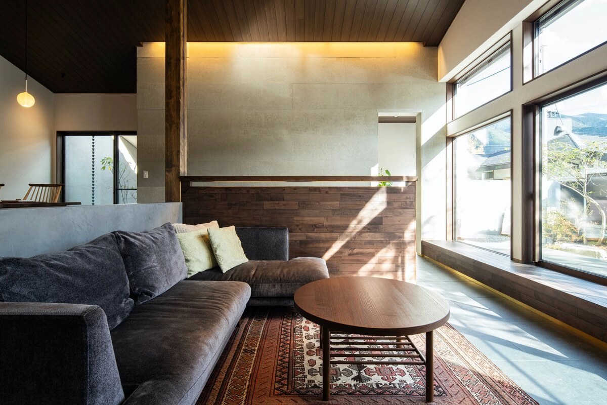 大きな窓から光が入り込む、落ち着いた色合いのソファと木の温もりに包まれたリビング