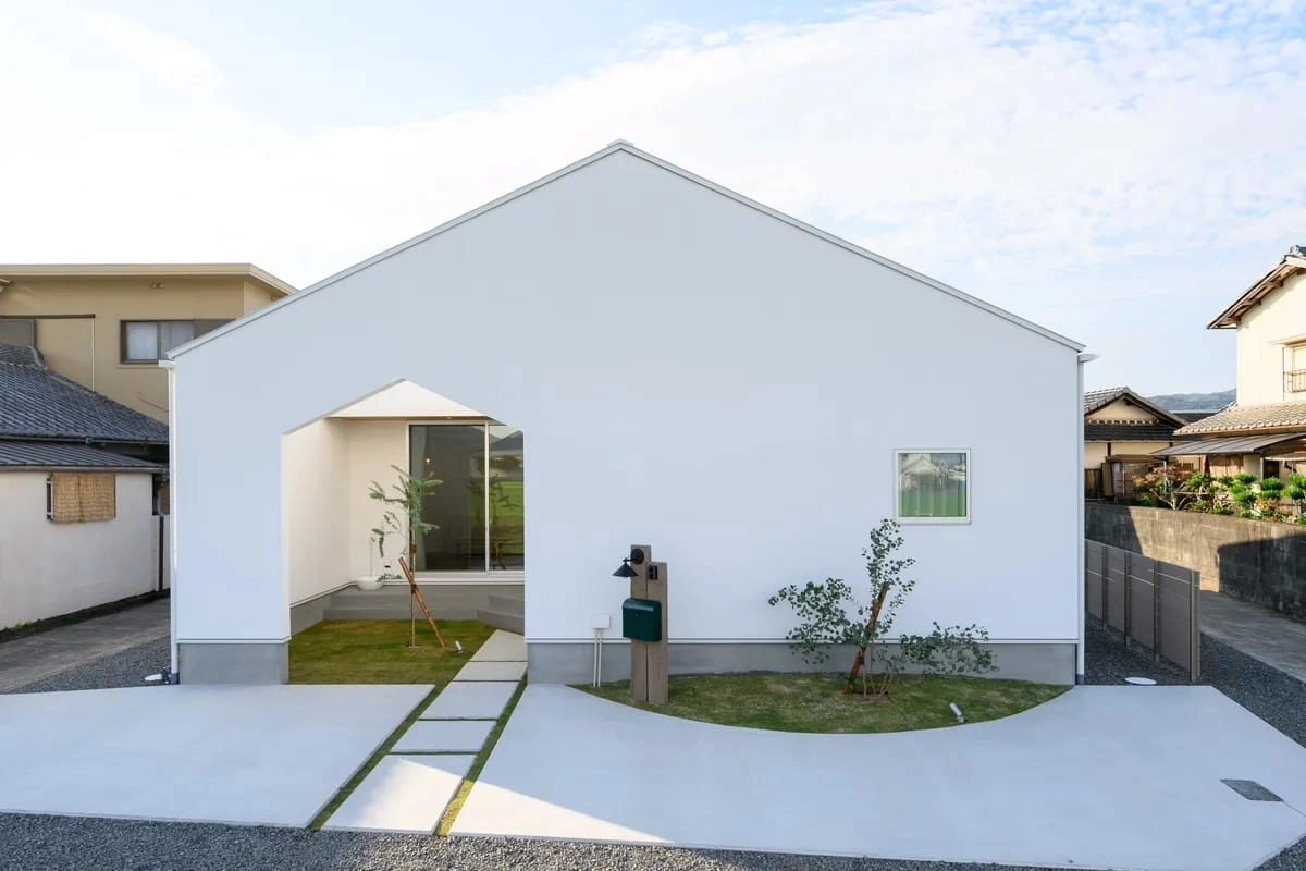 家型の入り口と芝生のアプローチがある白い平屋